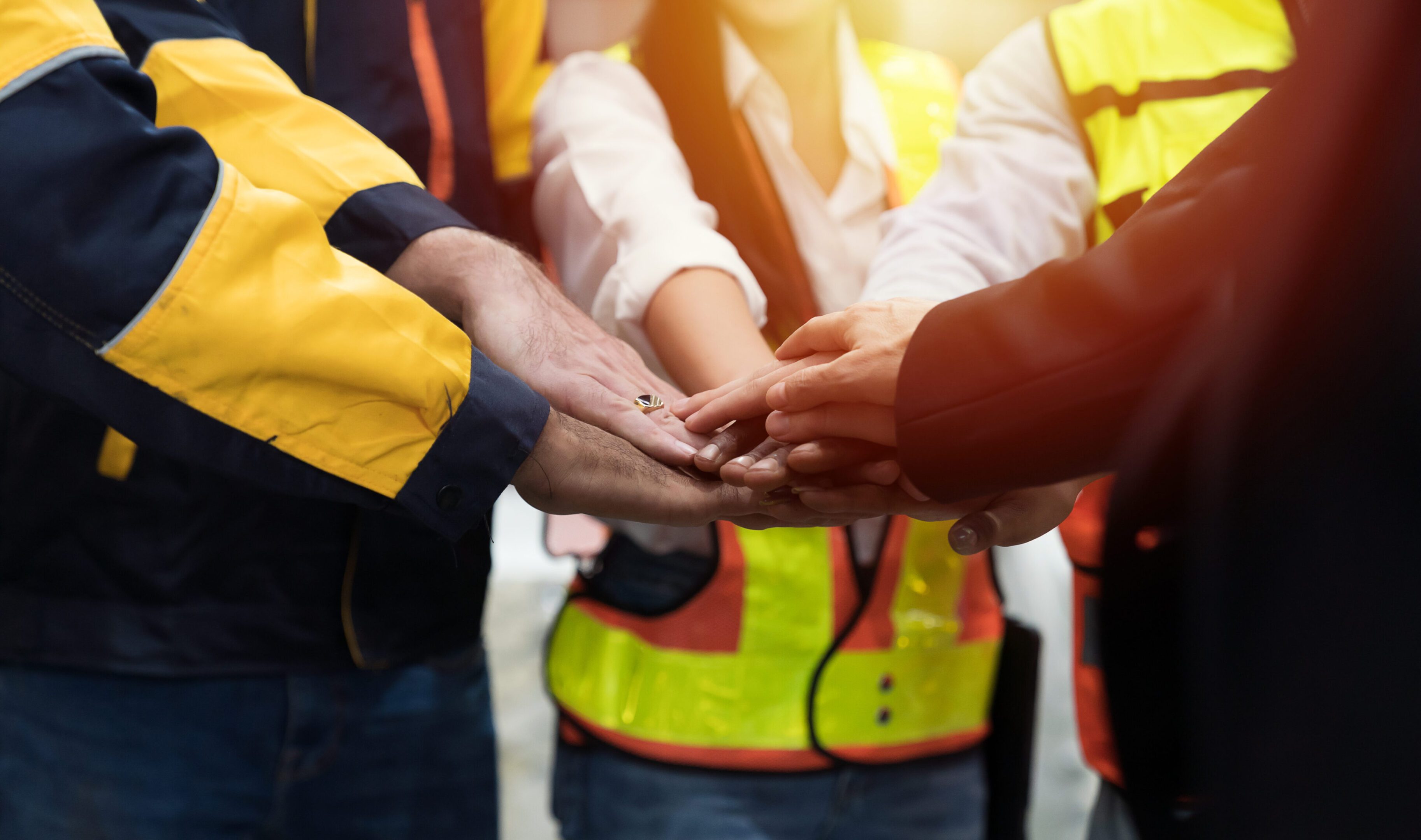 Group of male and female factory workers standing putting their hands together in industry factory. Factory workers stack of hands in factory. Unity and teamwork concept
