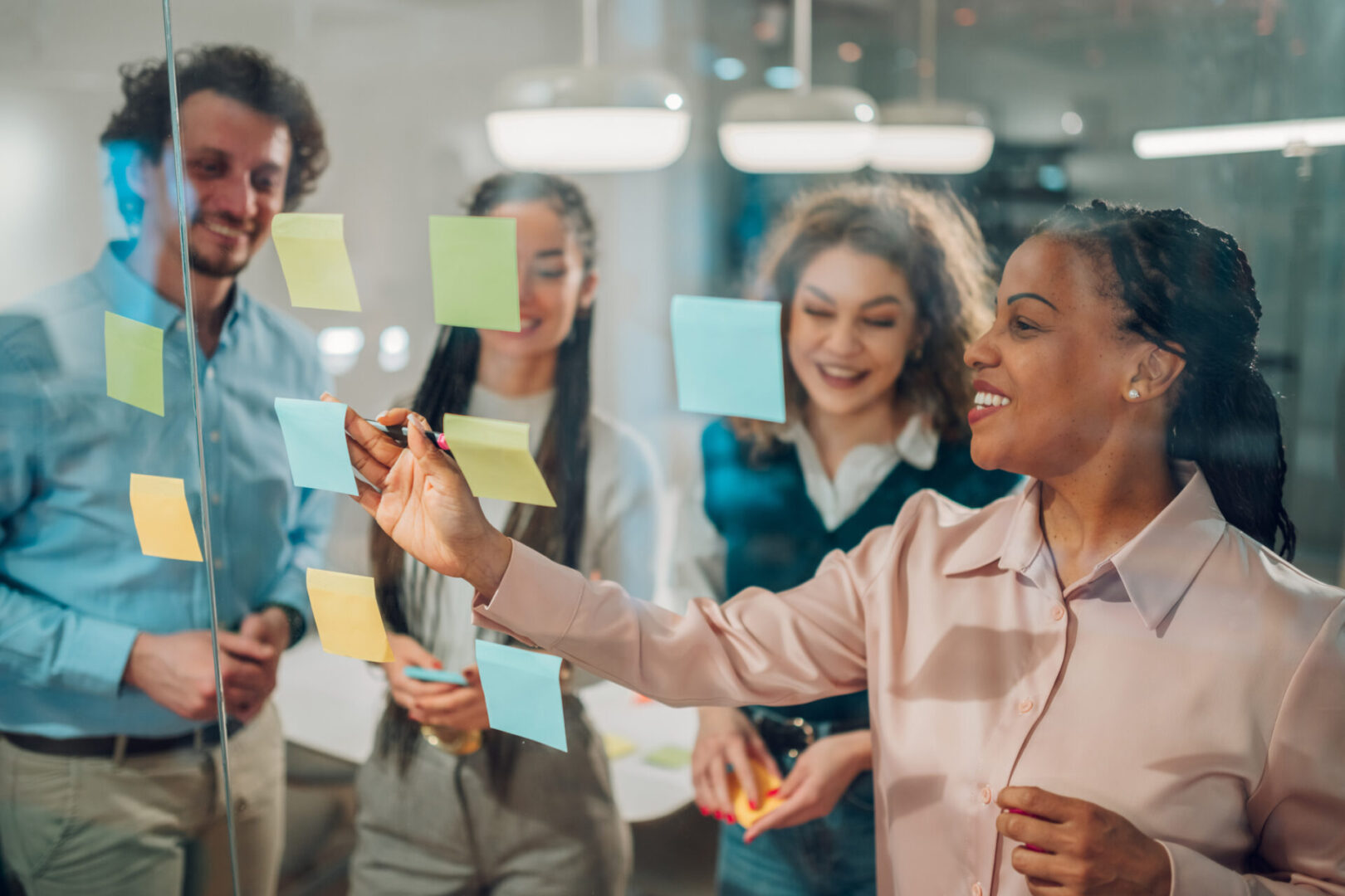 Diverse team collaborating on a project, using sticky notes on a glass wall in a modern office