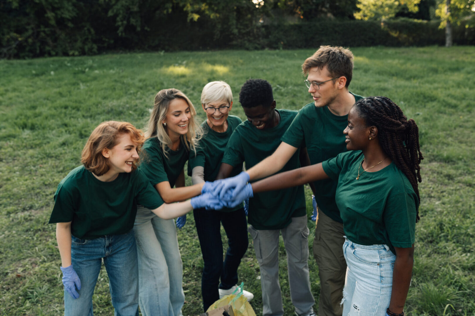 Group of volunteers joining hands in unity after successfully cleaning a park, demonstrating teamwork and commitment to environmental stewardship