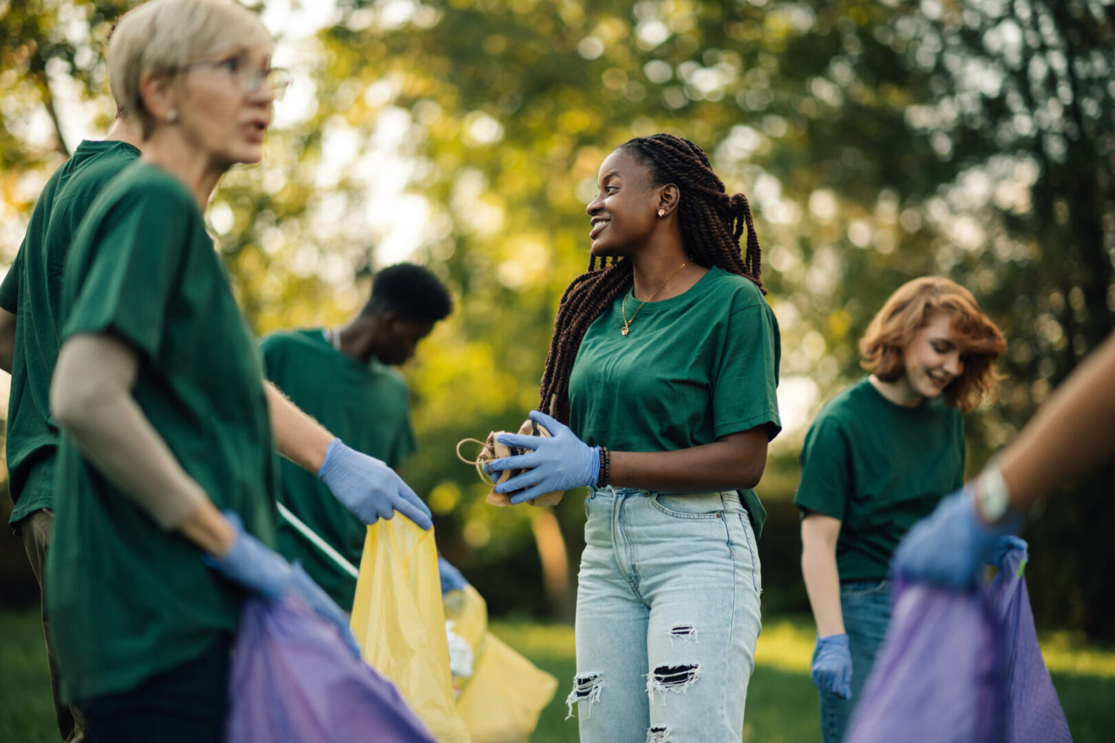 Group of diverse volunteers wearing green t-shirts and gloves collecting trash in park during community cleanup, promoting environmental awareness and teamwork