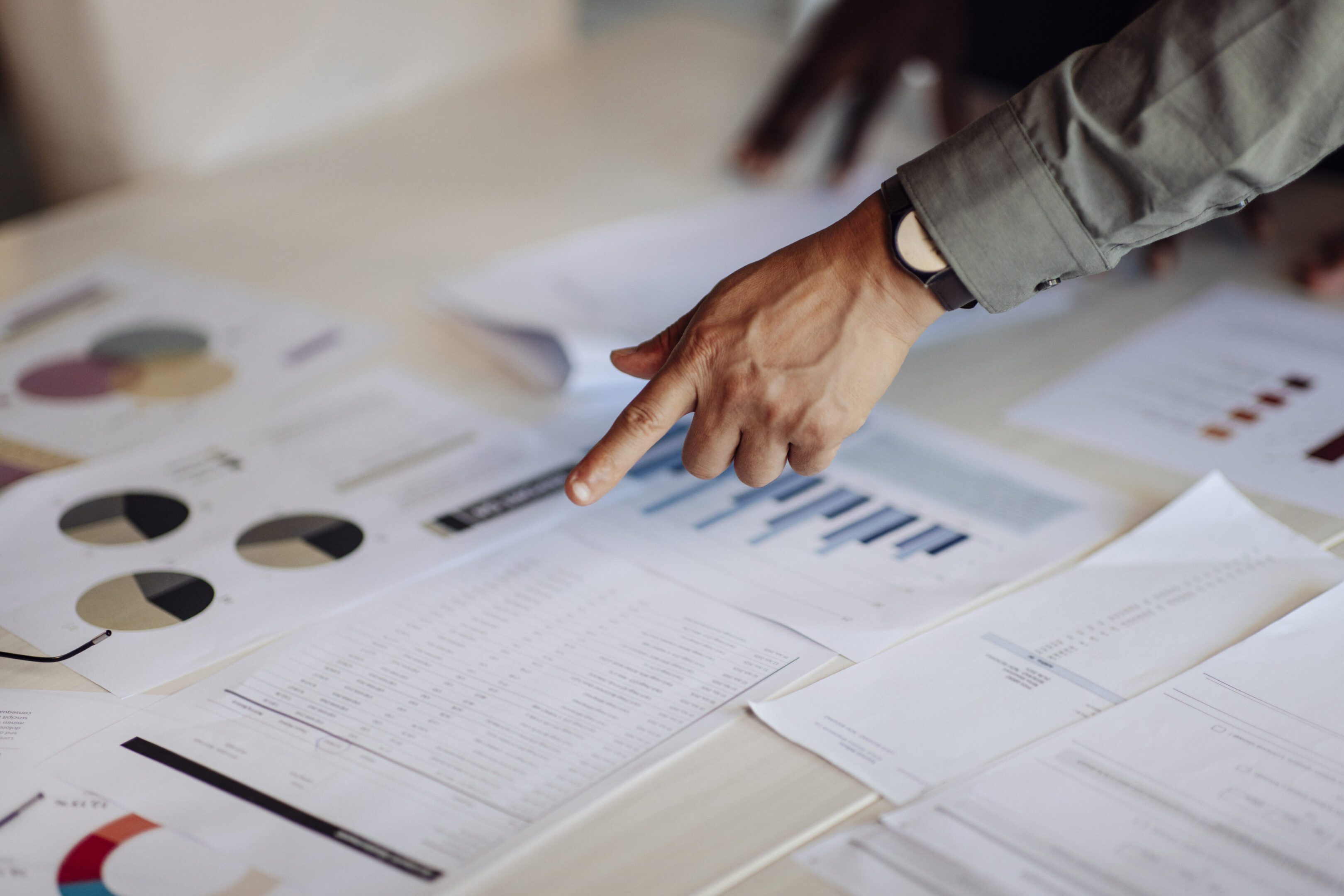 Hands pointing at charts and graphs on a table, reflecting collaboration, planning, and data-driven decision-making in a professional setting