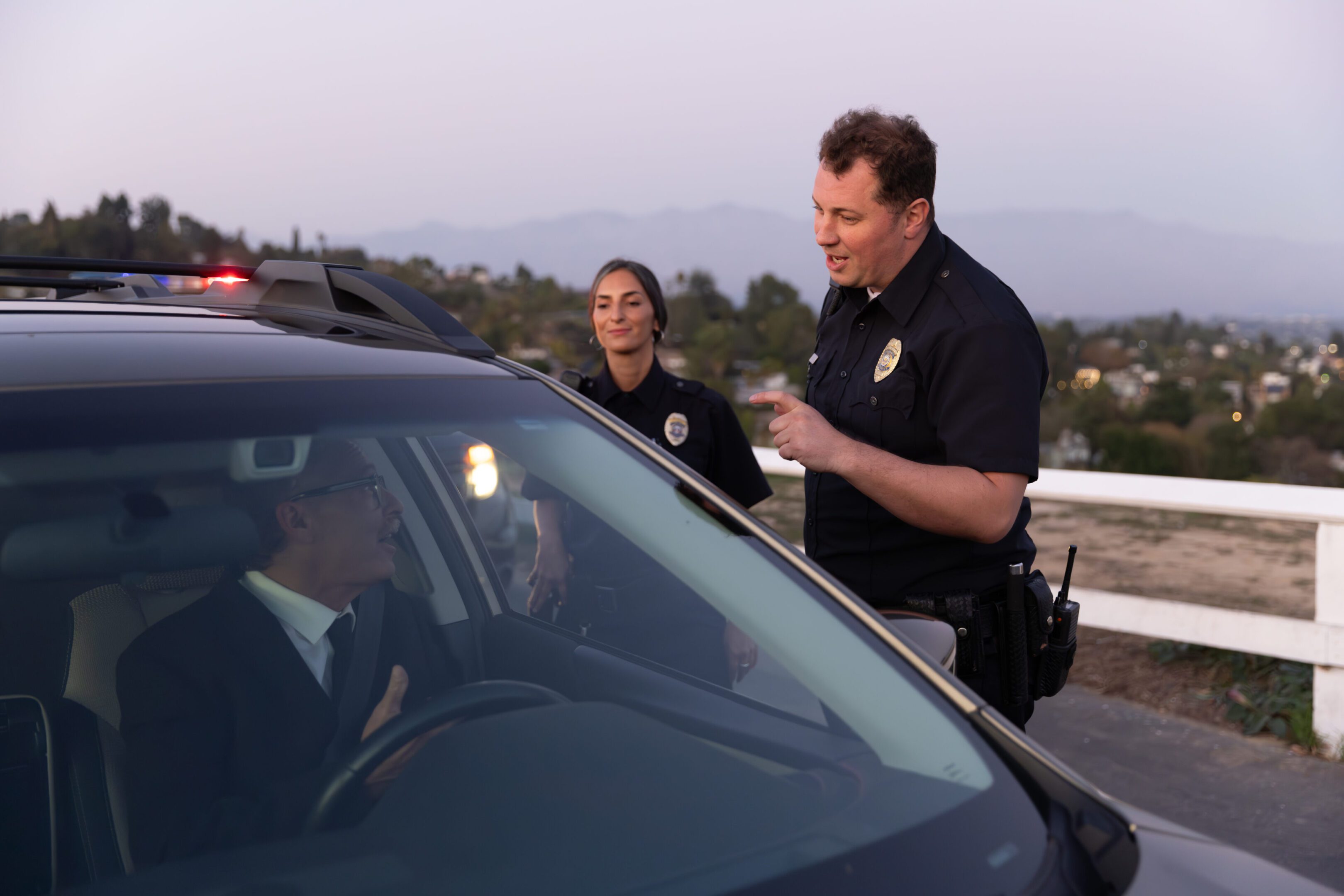 Shot of two police officers and a driver they pulled over on a scenic road at sunset.