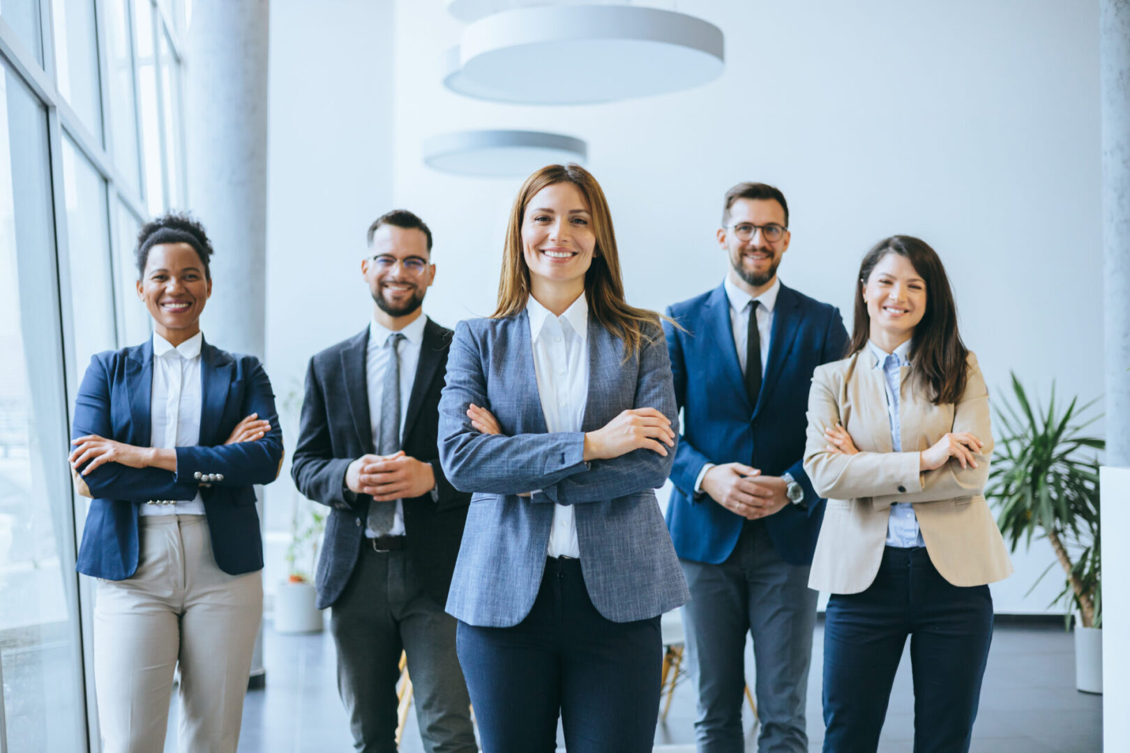 A team of business professionals stands with a confident woman in the lead, illustrating themes of leadership and cooperative teamwork in a corporate setting