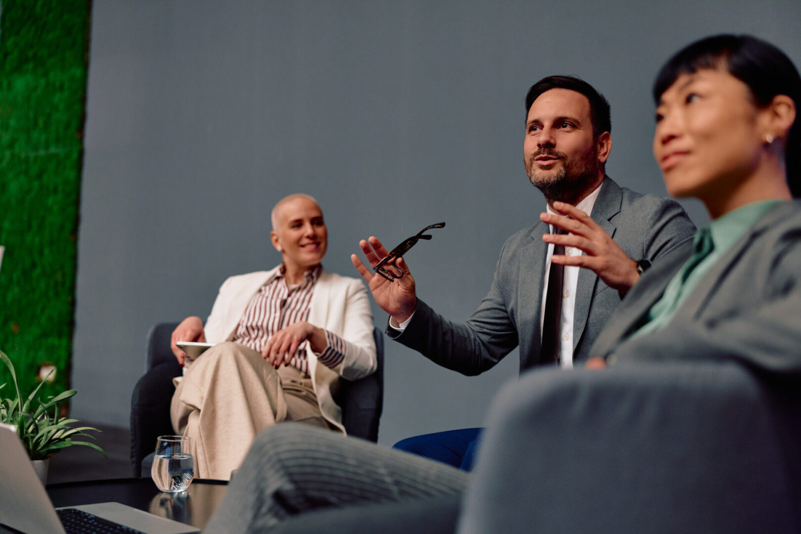 Group of business professionals actively participating in a corporate meeting, a man speaking and gesturing while two women intently listen, creating an atmosphere of collaboration and communication