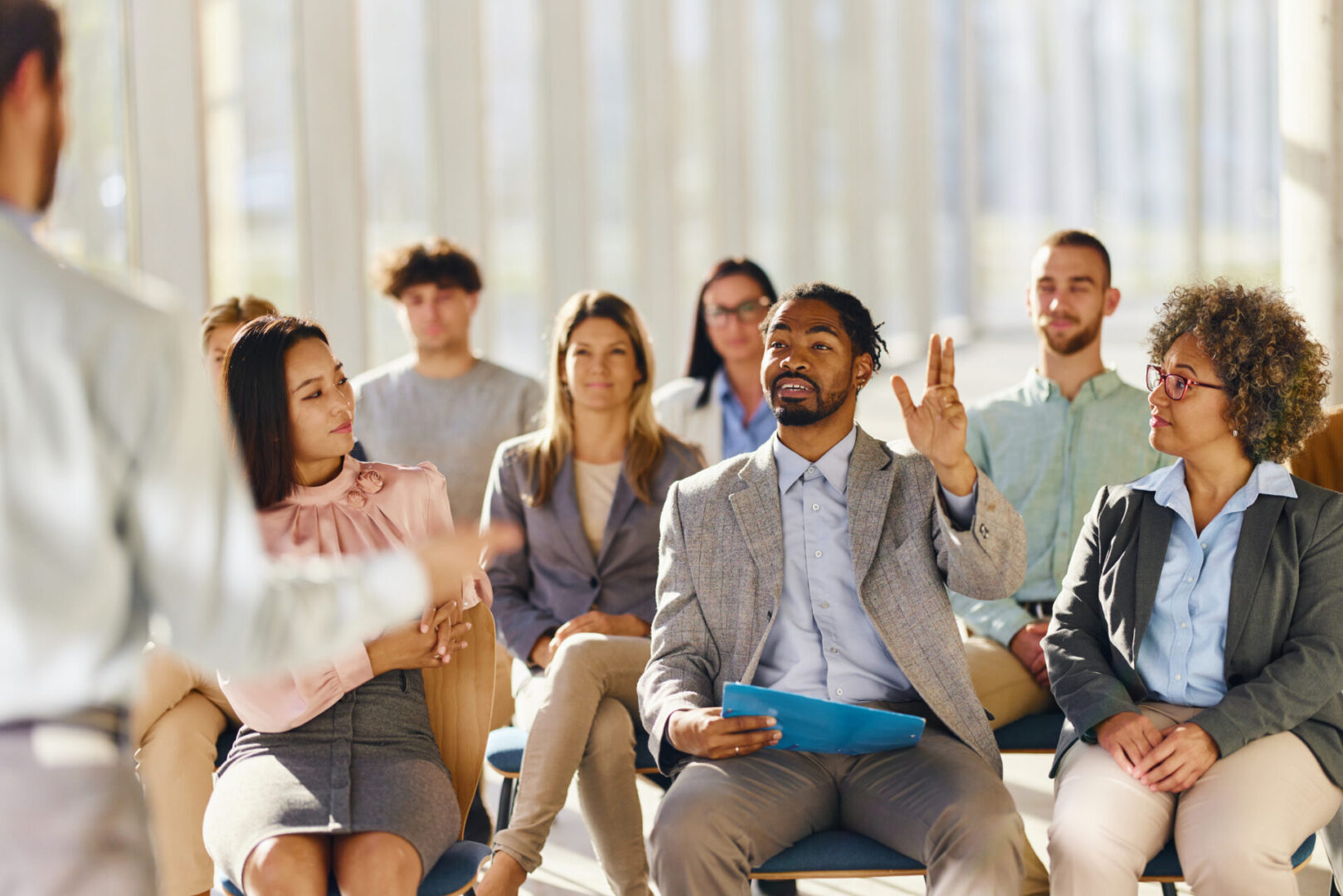 Happy black businessman wants to ask a question to a presenter during a seminar with his colleagues in a board room.