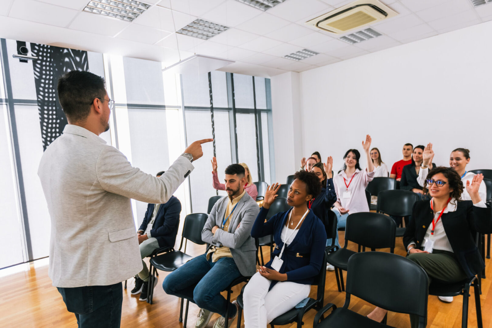 Male CEO standing in front of a multiracial group of colleagues and calls out someone to answer the question. Multimedia classroom with smart board.