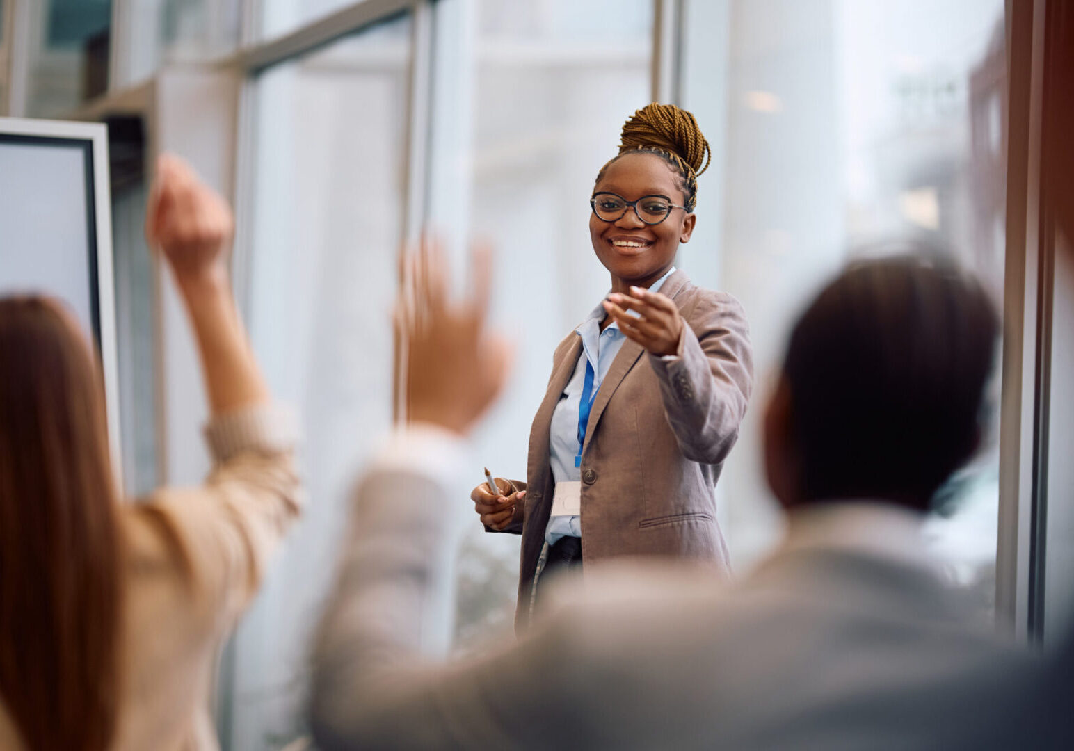 Happy African American businesswoman aiming at one of colleagues who wants to ask a question during a conference in board room.