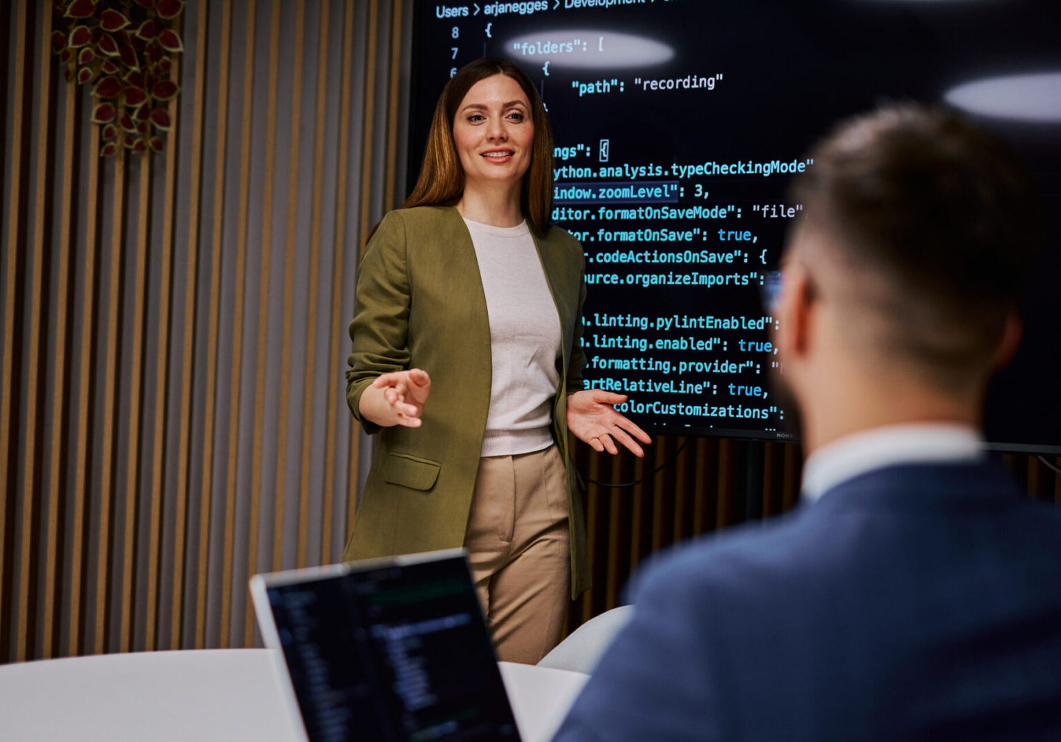 Female software developer is presenting code on a monitor to her colleague during a business meeting, discussing programming and development strategies
