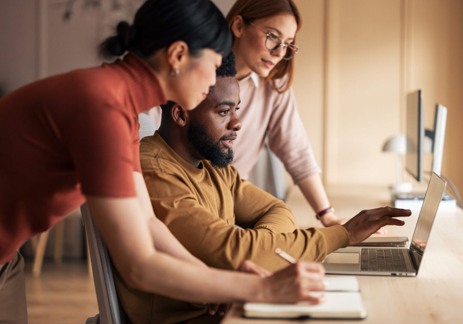 A team of professionals working collaboratively at a desk, utilizing a laptop for a shared project in a modern office. The environment reflects teamwork, collaboration, and productivity.