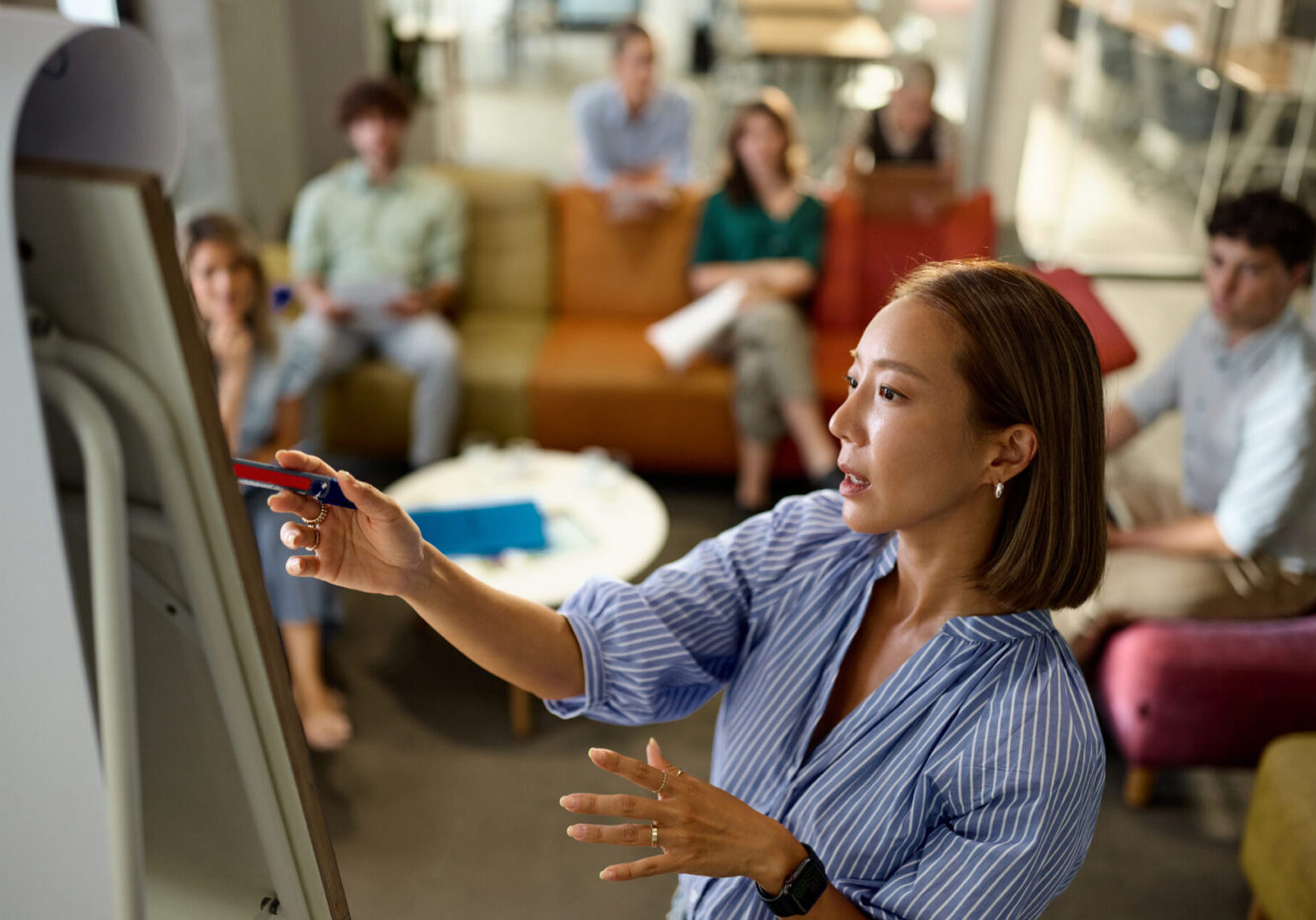 Korean businesswoman reading plans on whiteboard during sales pitch with her colleagues at casual office.