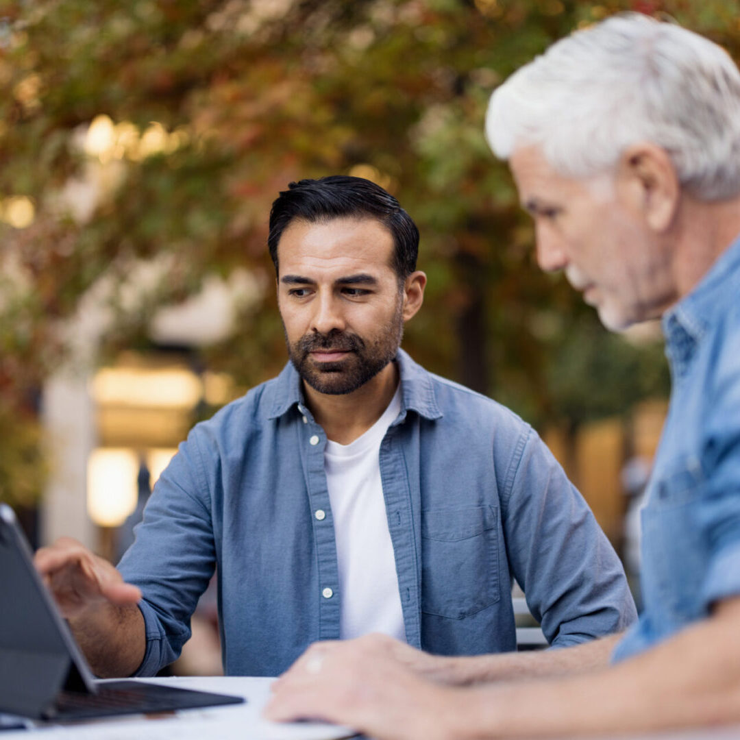 Two men collaborating and sharing ideas outdoors, using a digital tablet for work and communication in an autumn setting